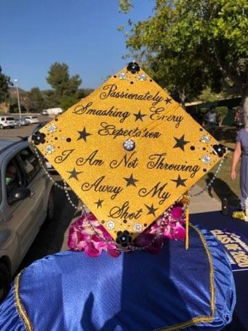 Graduation cap decorated in gold and quotes from Hamilton